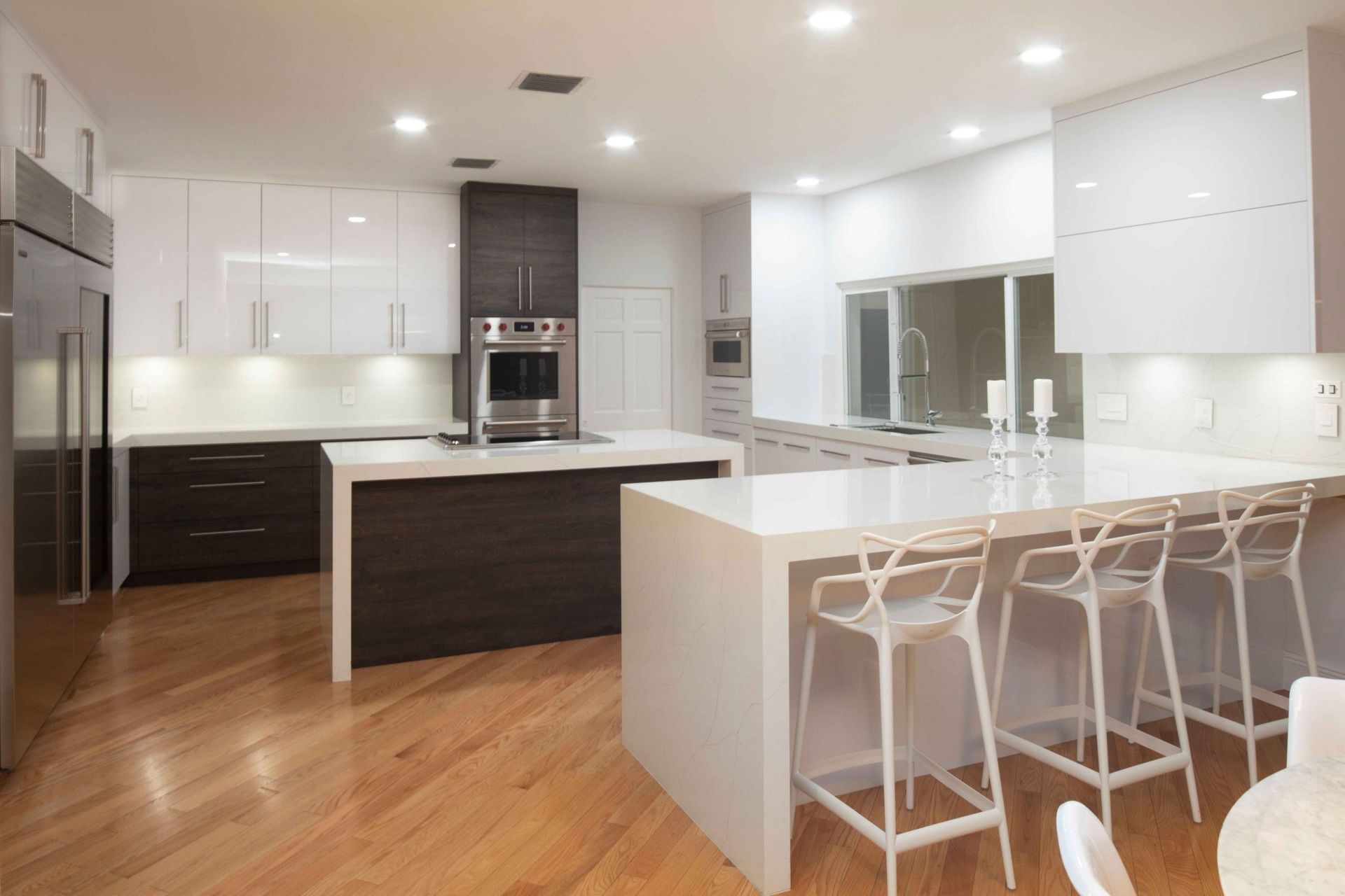Modern white kitchen with island, bar stools, wood floors, and built-in appliances
