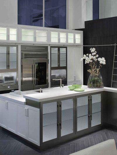 Modern kitchen with white cabinets, glass-front island, and dark accent wall, lit by frosted upper windows