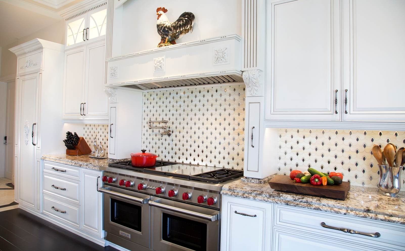 Bright white kitchen with gas range, granite counters, decorative rooster above the stove, and fruit on the counter