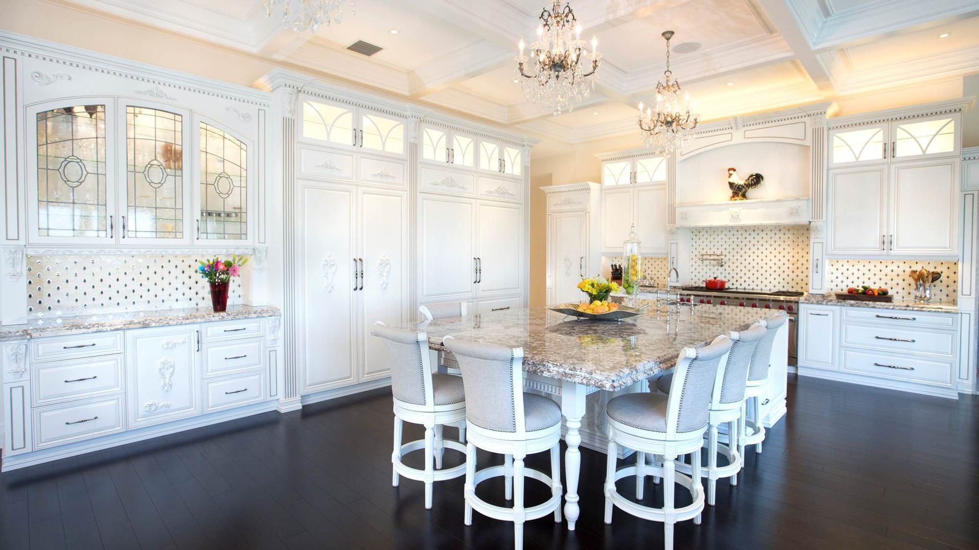 Bright white kitchen with ornate cabinets, dark floors, and a marble island set with white chairs