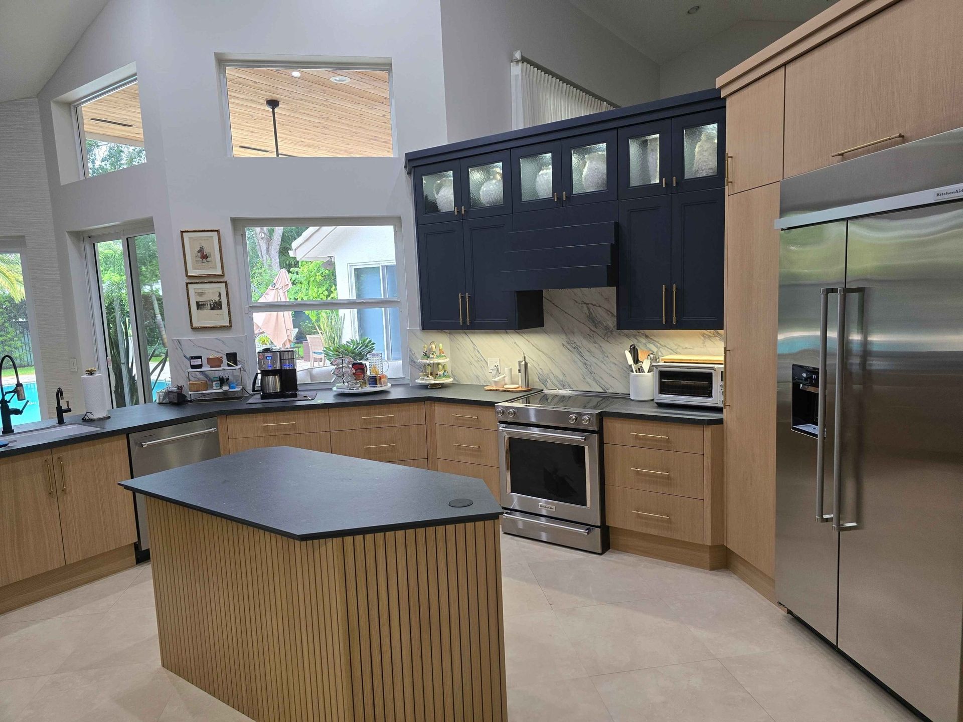 Modern kitchen with dark blue cabinets, stainless steel appliances, and a central island by bright windows