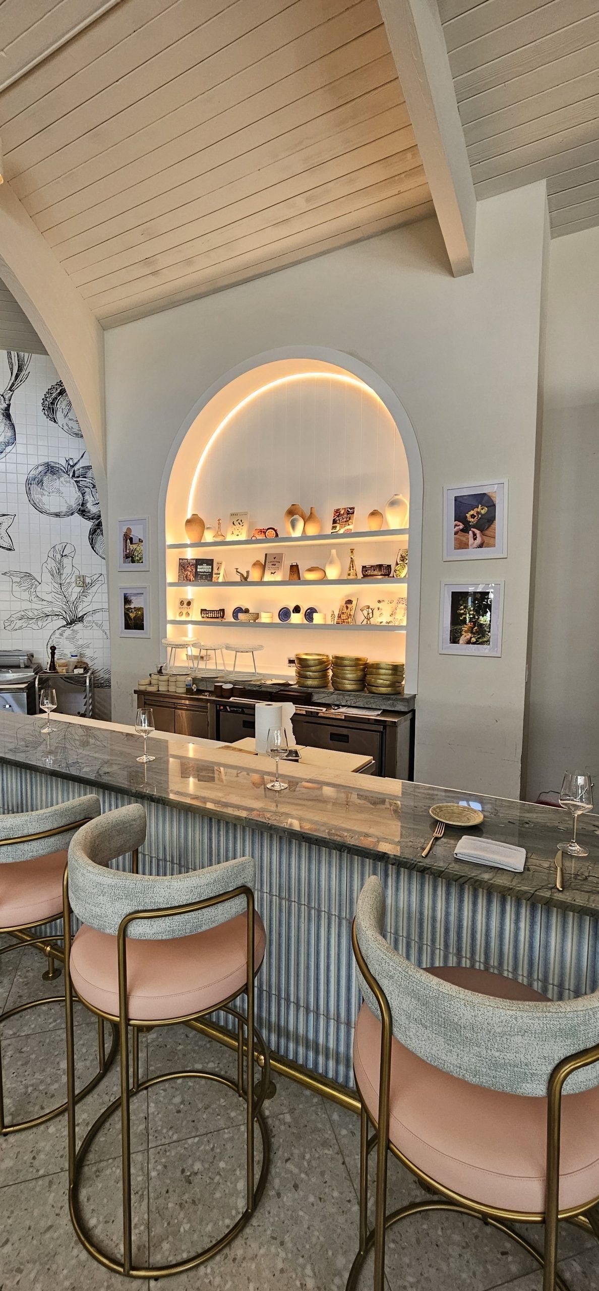 Stylish bar with arched backlit shelves, marble counter, and rattan barstools in a pastel lounge