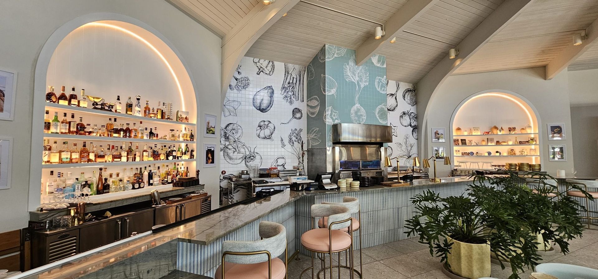 Bright modern café interior with arched backlit shelves, a curved bar, and leafy plants