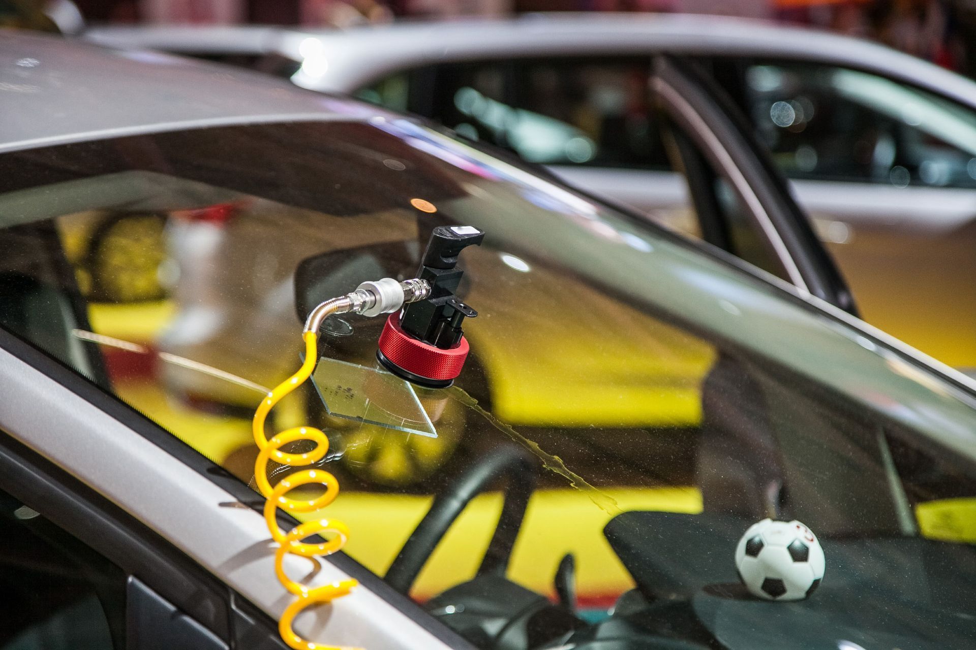 A windshield crack being repaired with a device, yellow hose, and soccer ball on dashboard.
