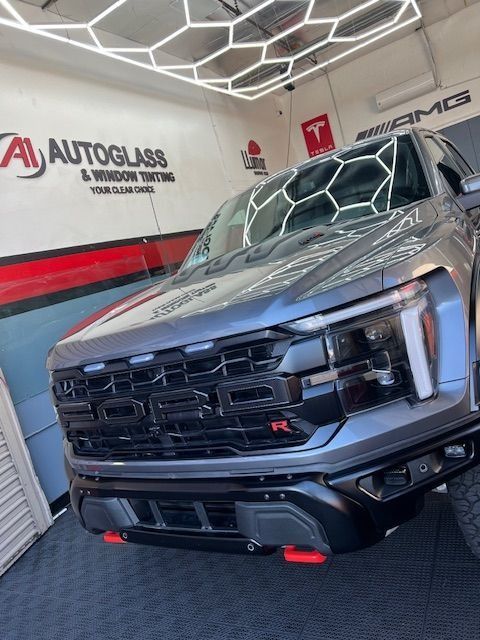 Gray Ford Raptor truck with black grille and red accents parked inside a shop with bright lights.