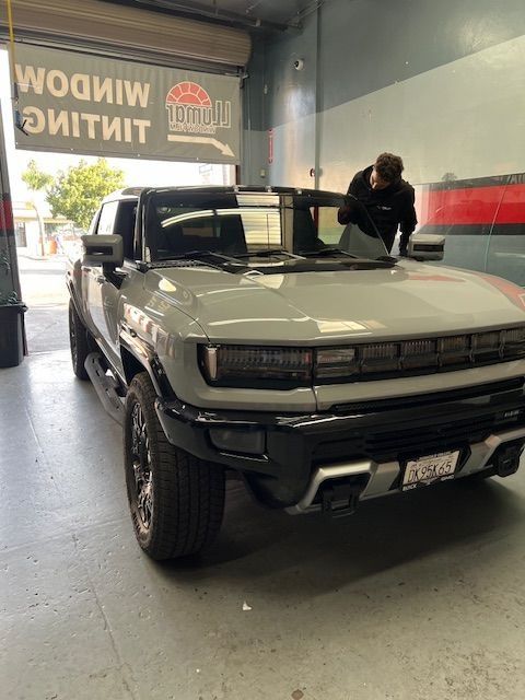 A light gray Hummer EV truck being worked on inside a window tinting shop.