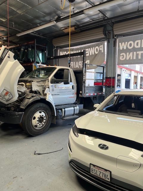 White truck with open hood next to white car in a repair shop.