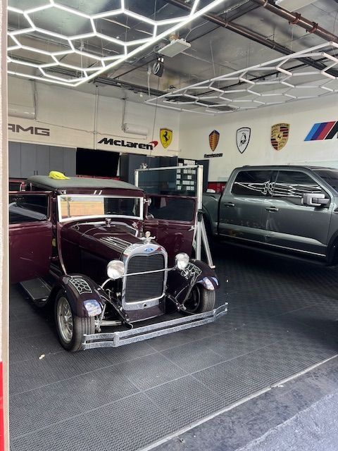 Classic car and modern truck in a garage with luxury car brand emblems on the wall.