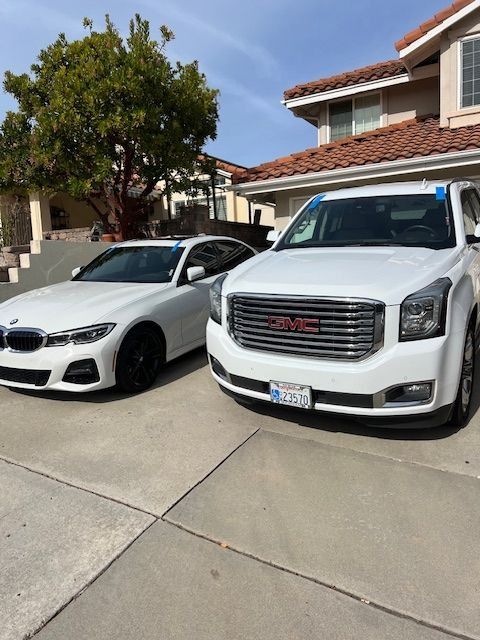 Two white cars parked in front of a house: a BMW sedan and a GMC Yukon SUV.