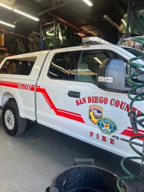 White San Diego County Fire truck in a garage; red stripe and logos on side.