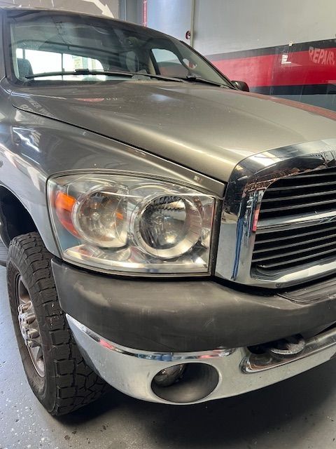 Gray Dodge Ram pickup truck's front with chrome grill, bumper, and headlight.