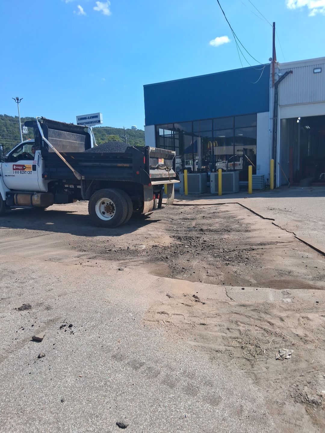 Dump truck parked at a building, unloading gravel onto a dirt surface under a blue sky.