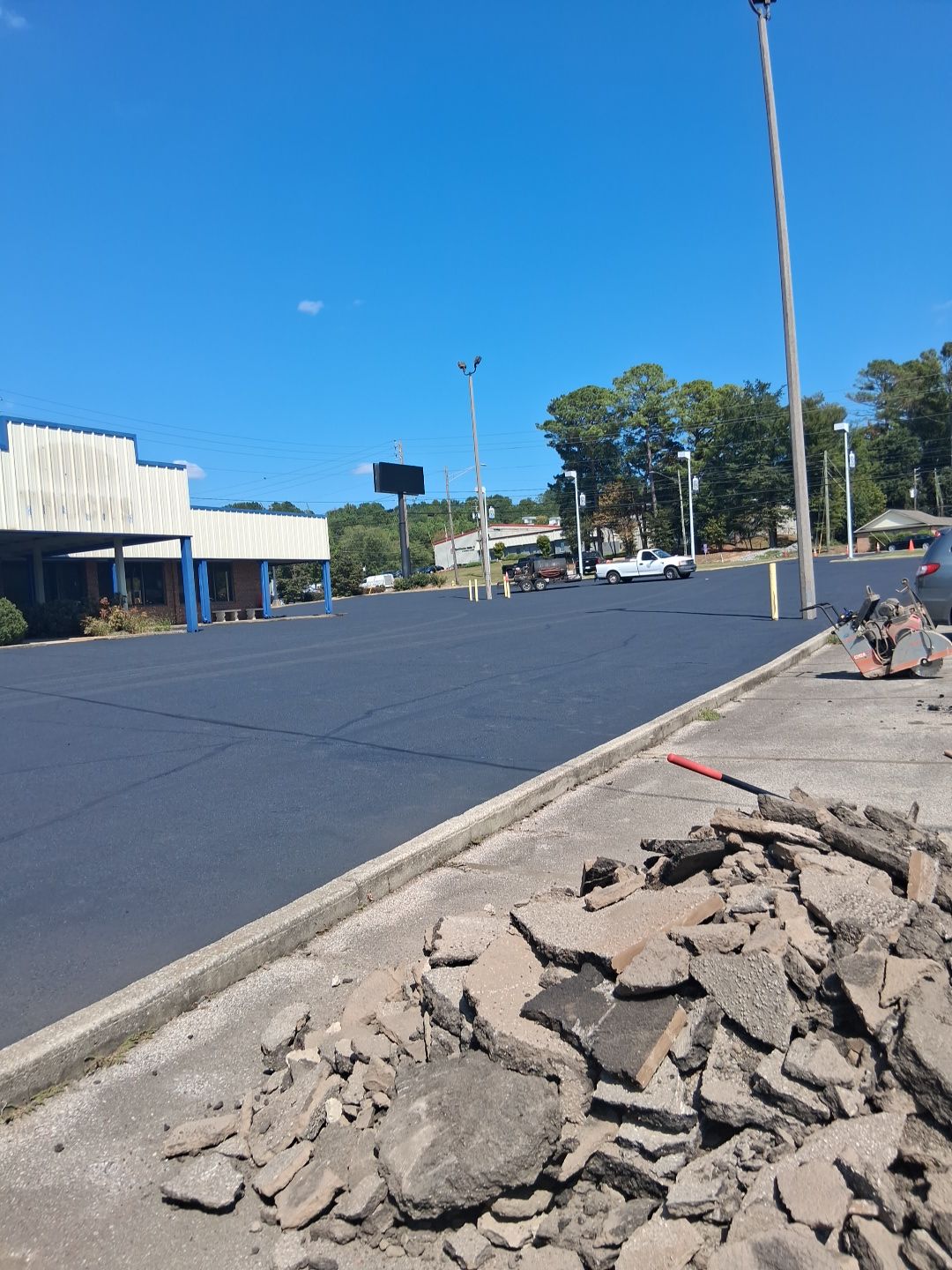 Newly paved asphalt parking lot; construction debris in foreground. Clear blue sky.