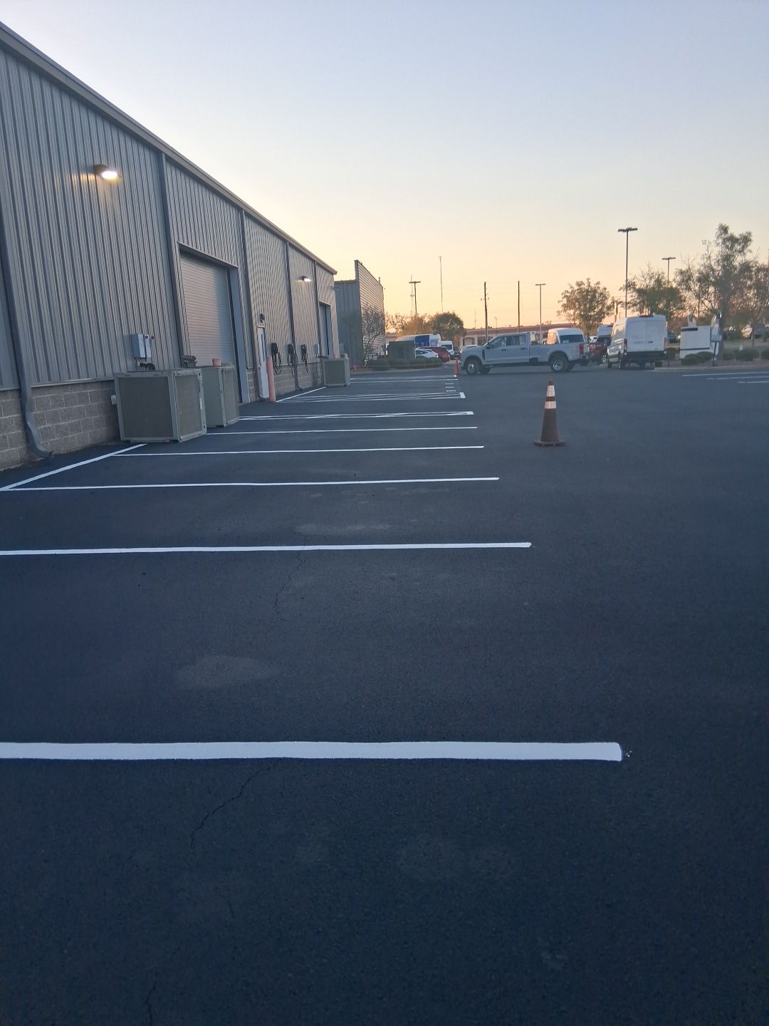 Parking lot with white lines, a building with bay doors, and a traffic cone.
