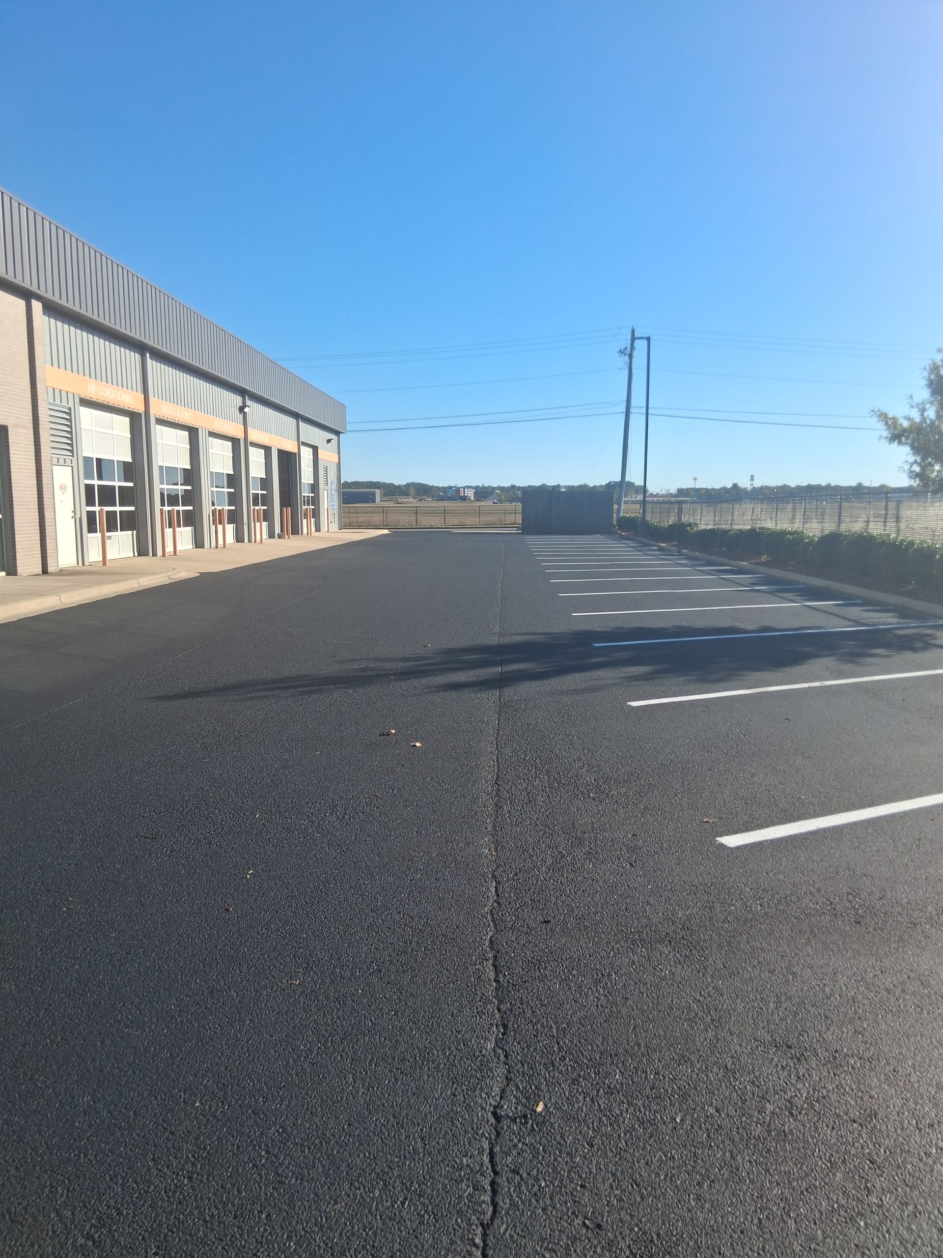 Exterior of a building with a newly paved asphalt parking lot on a sunny day.