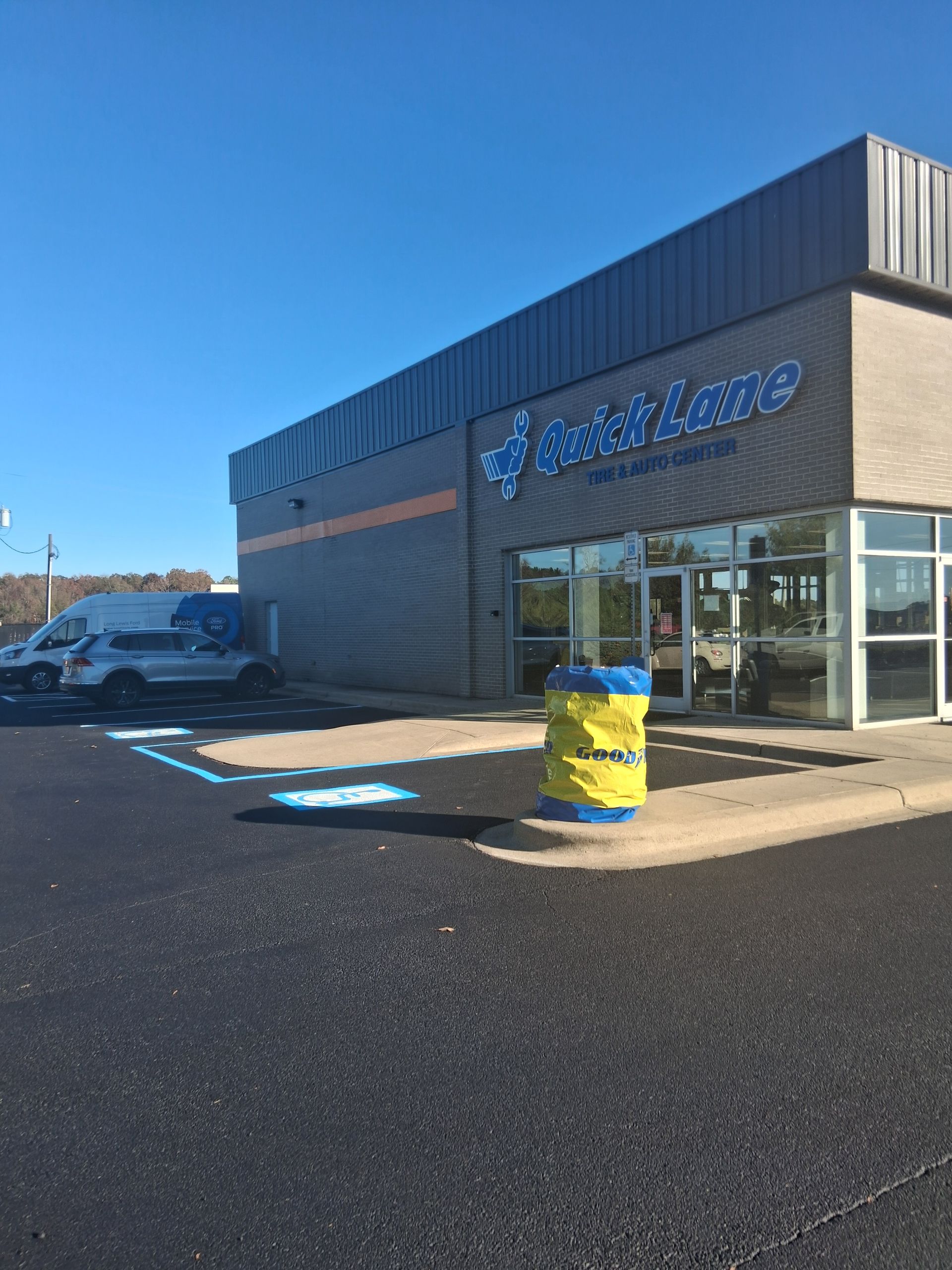 Exterior view of a Speed Lube building with a blue and yellow wrapped trash can and vehicles parked outside.