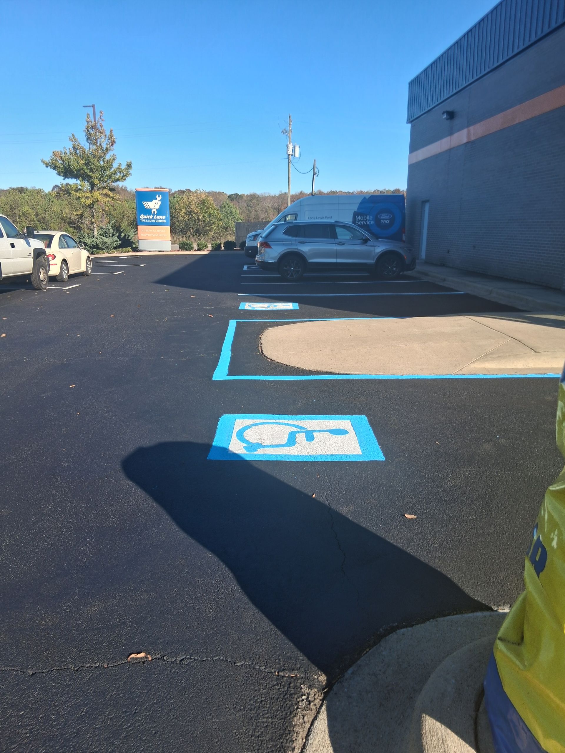 Blue wheelchair accessible parking spaces in a newly paved parking lot, with a building and vehicles.