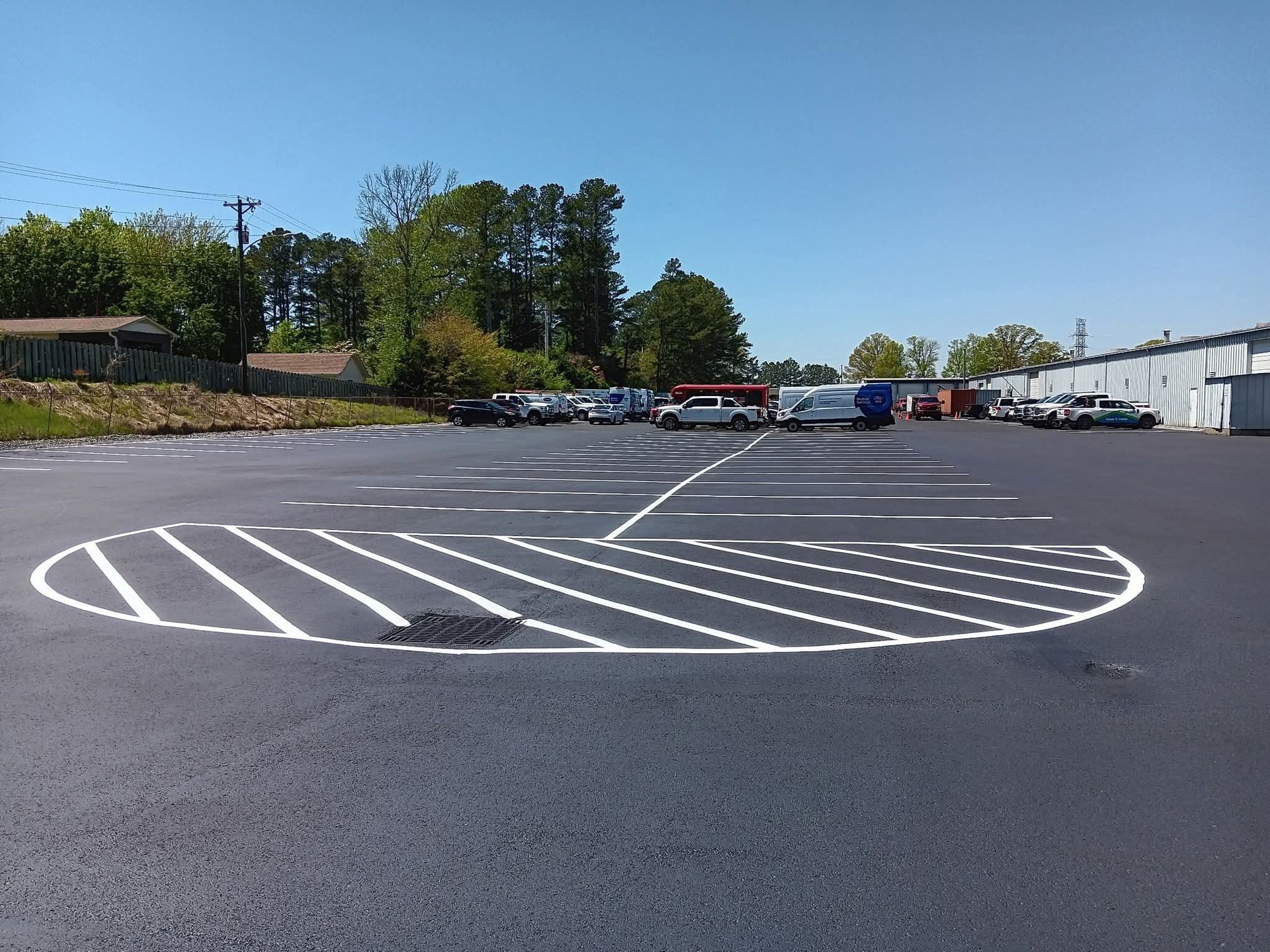 Asphalt parking area with painted white lines creating a large pie chart shape, and cars parked in the distance.