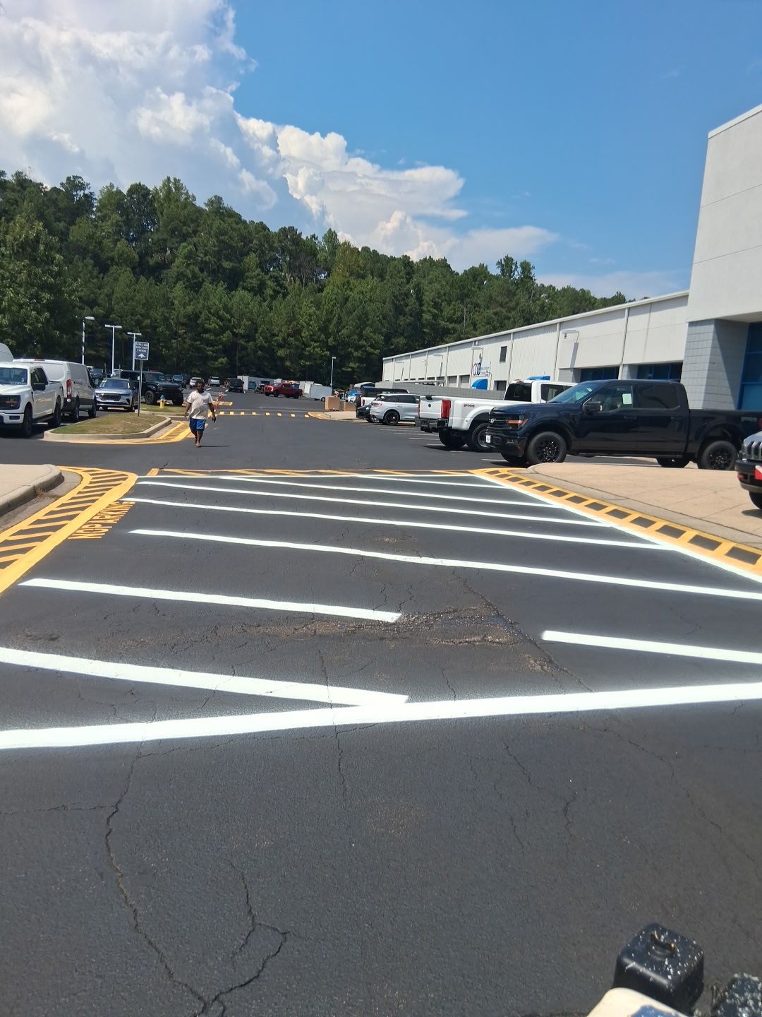 Crosswalk with white and yellow markings. Trucks and vans parked nearby. Person walking in the distance. Blue sky.