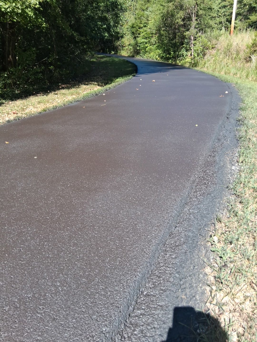 Black asphalt path winding through a grassy area, trees in the background.