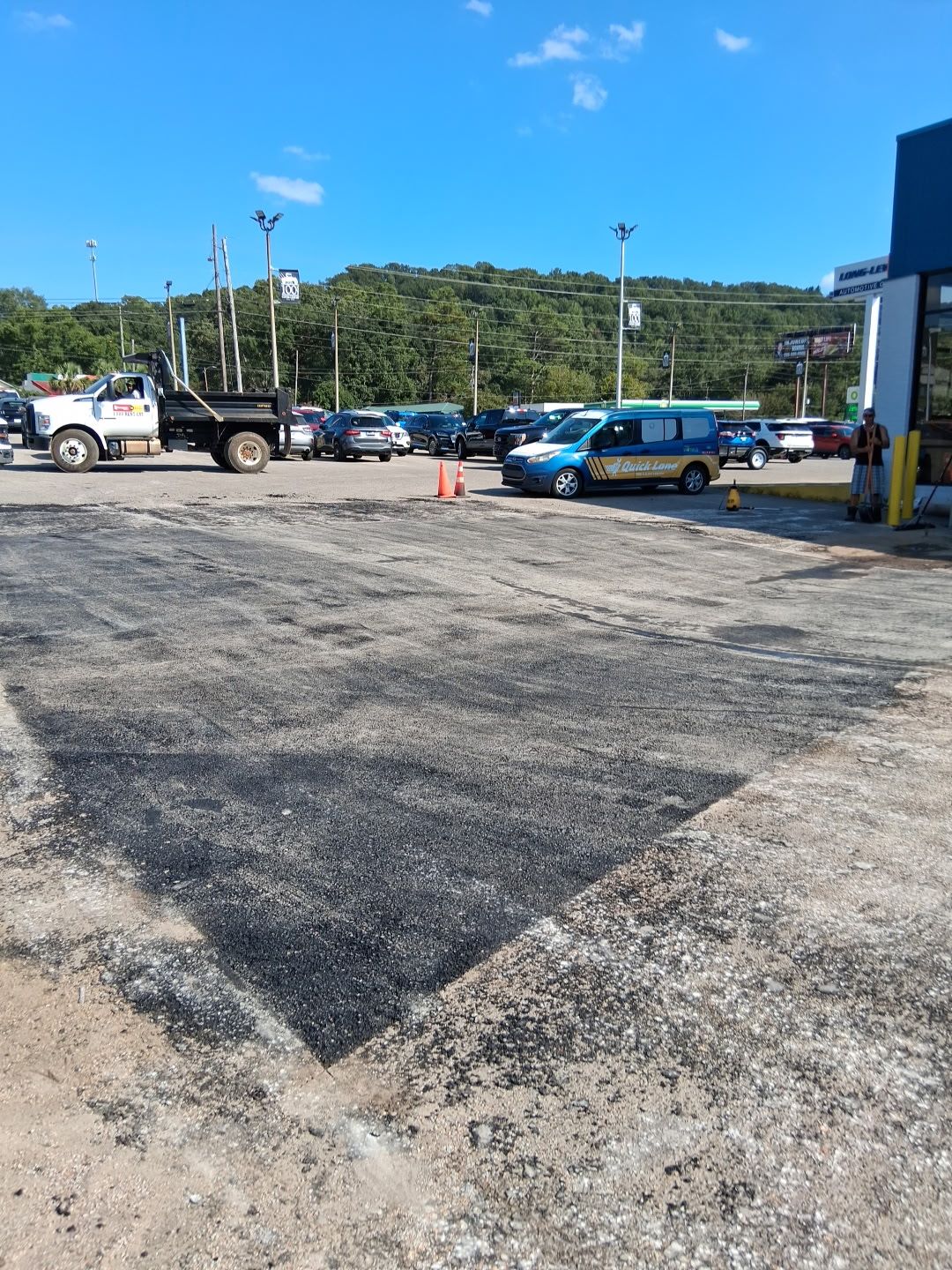 Asphalt repair in a parking lot, with a truck, cars, and a hill in the background.