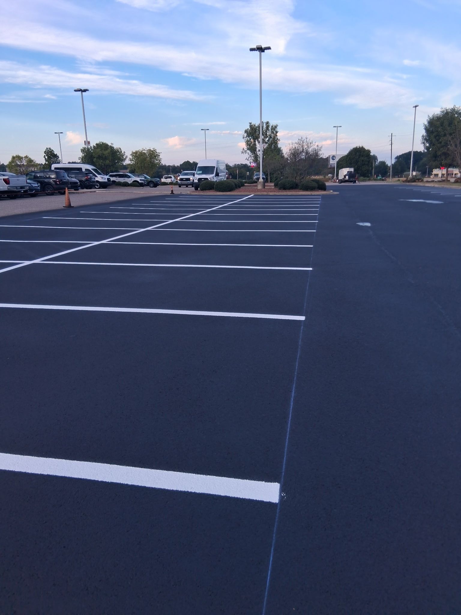 Empty parking lot with white painted lines and parked cars in the distance.