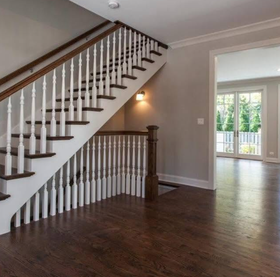 Staircase with white spindles and wood railing in an empty living room with hardwood floors