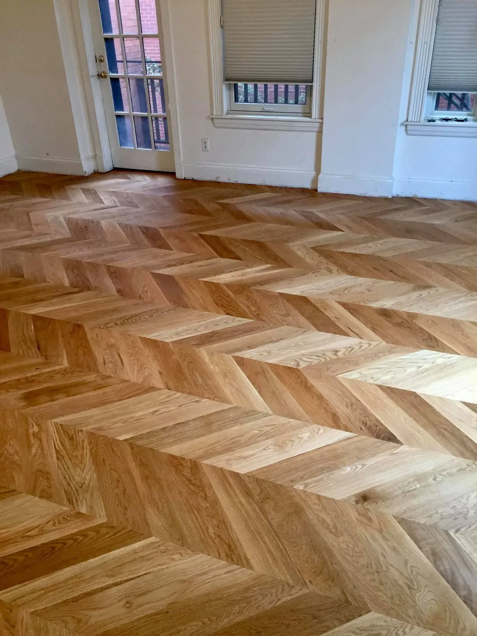 Empty room with herringbone wood floor and windows along the wall