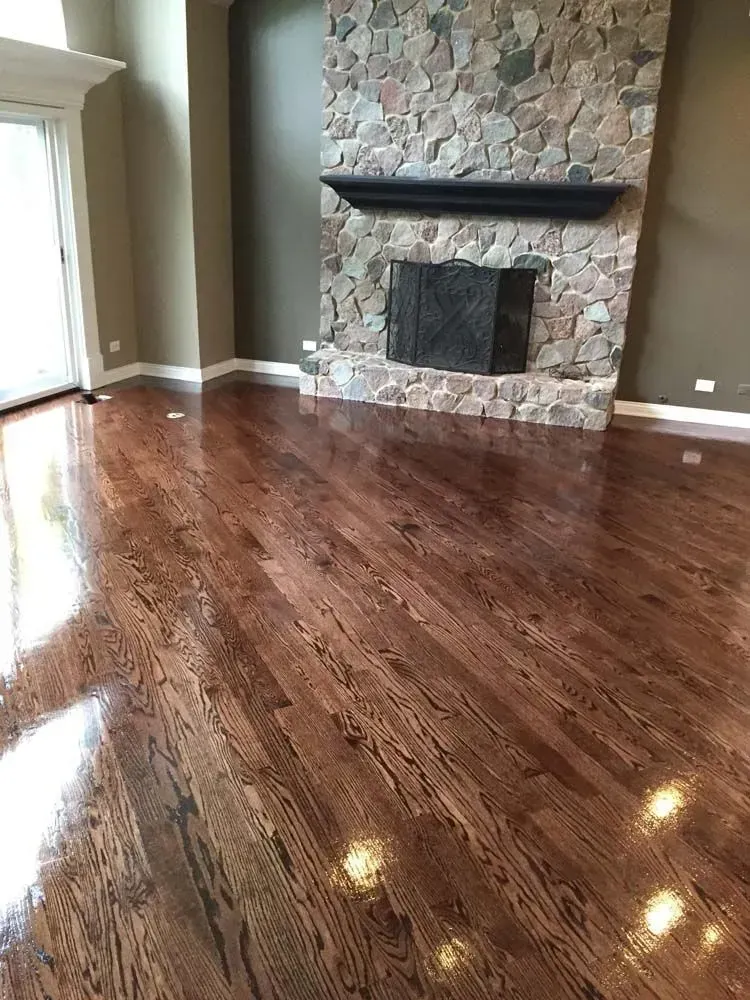 Empty living room with polished hardwood floors, stone fireplace, and sliding glass doors.