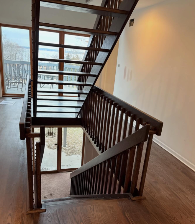 Interior stairwell with dark wood railing and open risers beside a large window overlooking snow.
