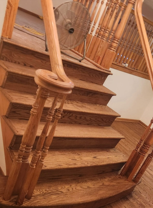 Wooden staircase with carved banister and a large standing fan in the hallway