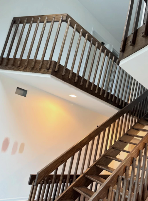 Indoor wooden staircase with dark railings and white walls, viewed from below.