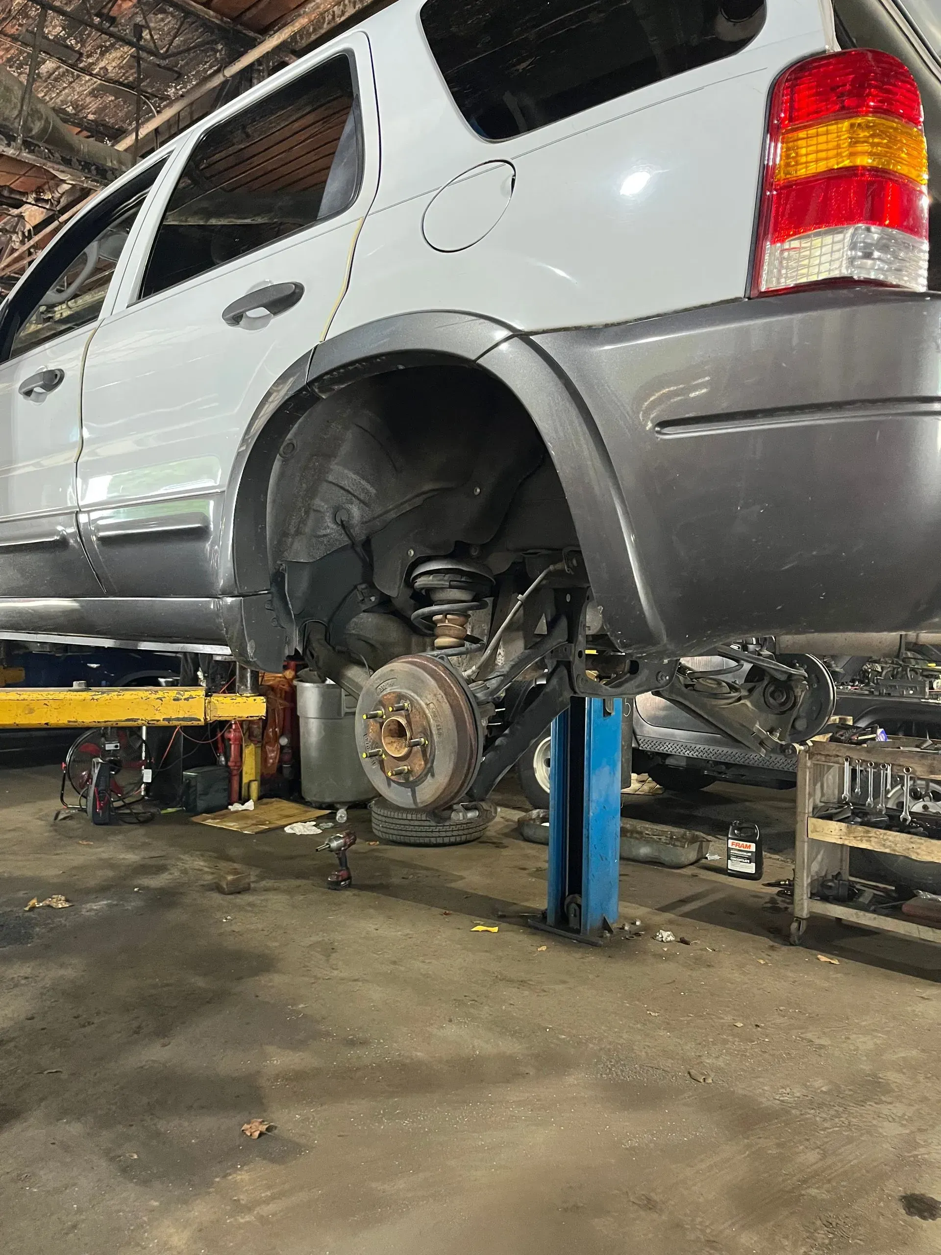 Silver SUV on a lift in a garage, rear wheel removed, exposing brake components.