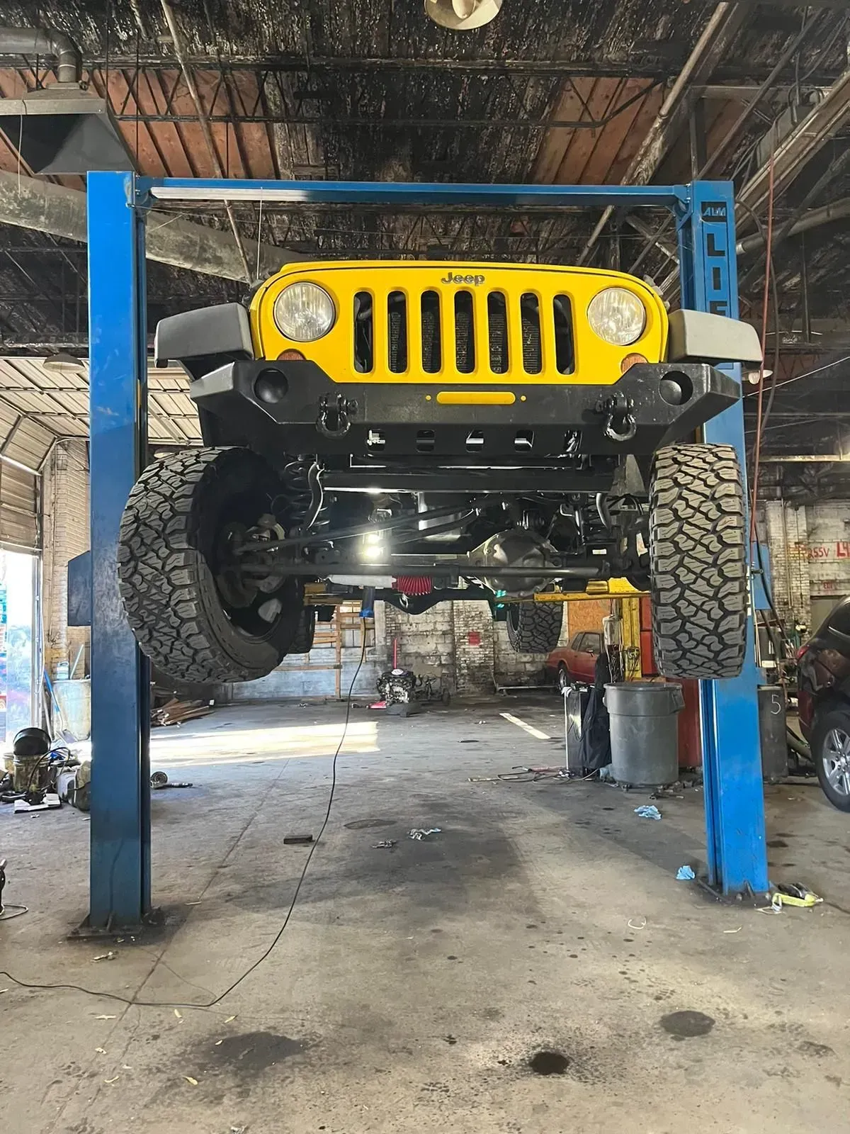 Yellow Jeep on a blue car lift inside a garage.