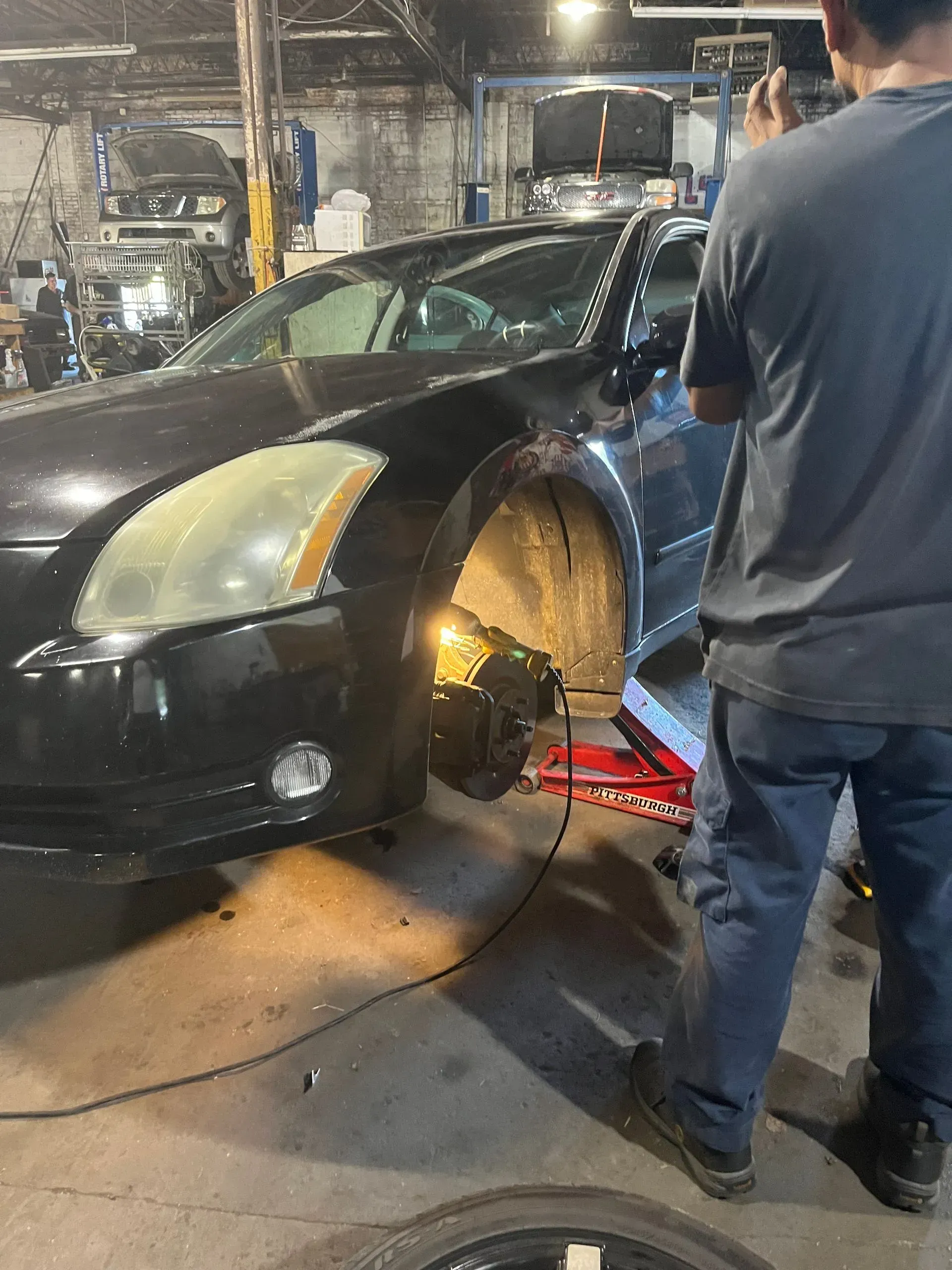 A car with front wheel removed in a mechanic shop. A person stands nearby.