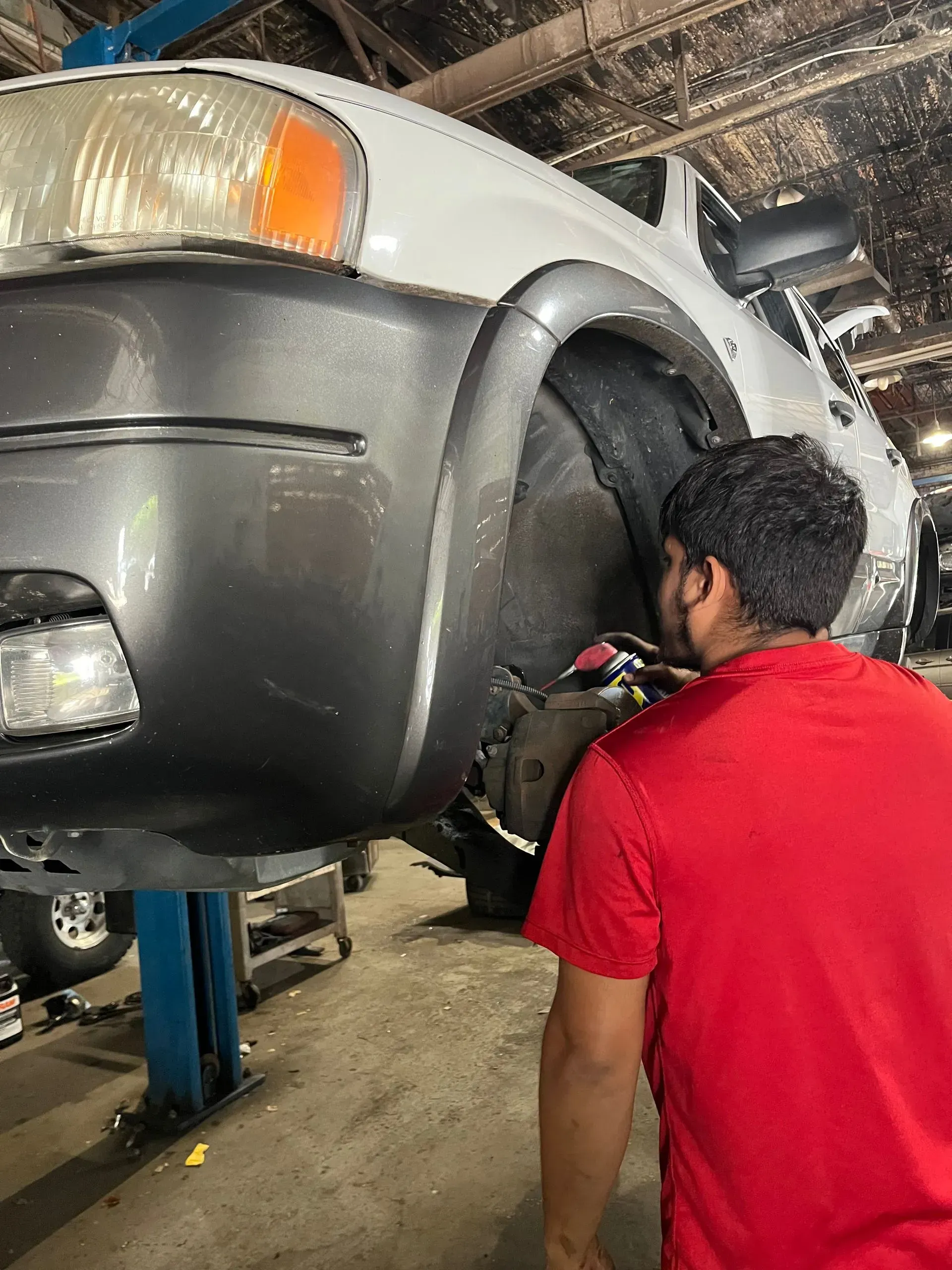 Man in red shirt working on a car raised on a lift in a repair shop.