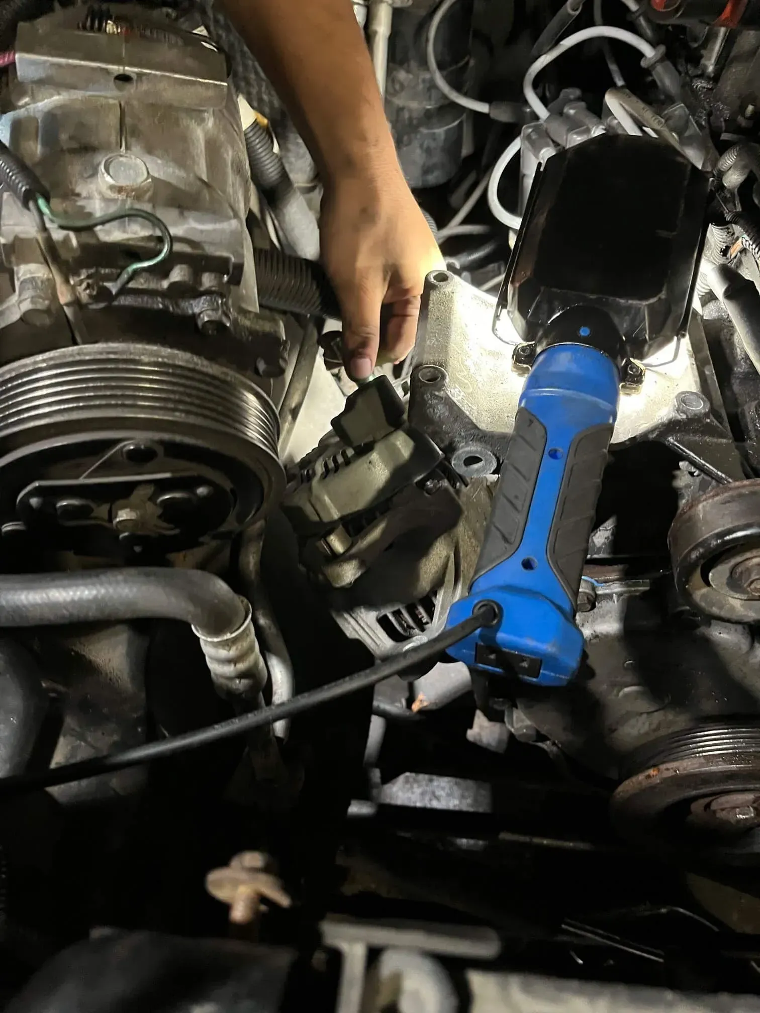 Hand working on car engine, illuminated by a blue and black work light.