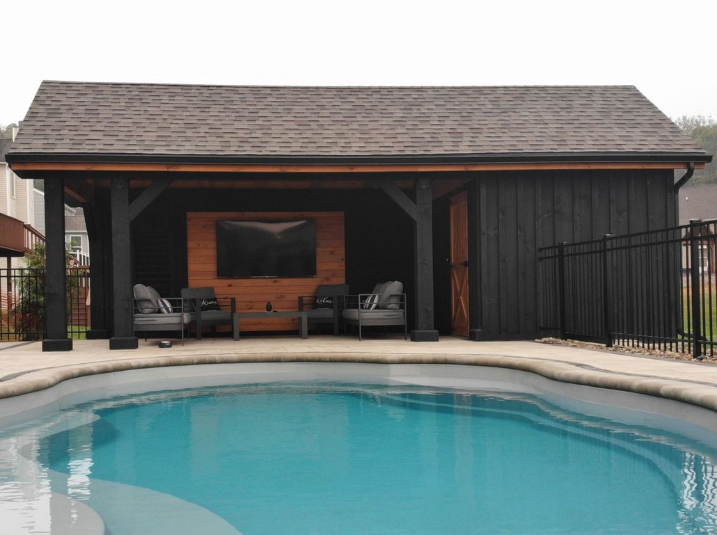 House with a pool and solar panels on the roof on a sunny day. A deck with lounge chairs is nearby.