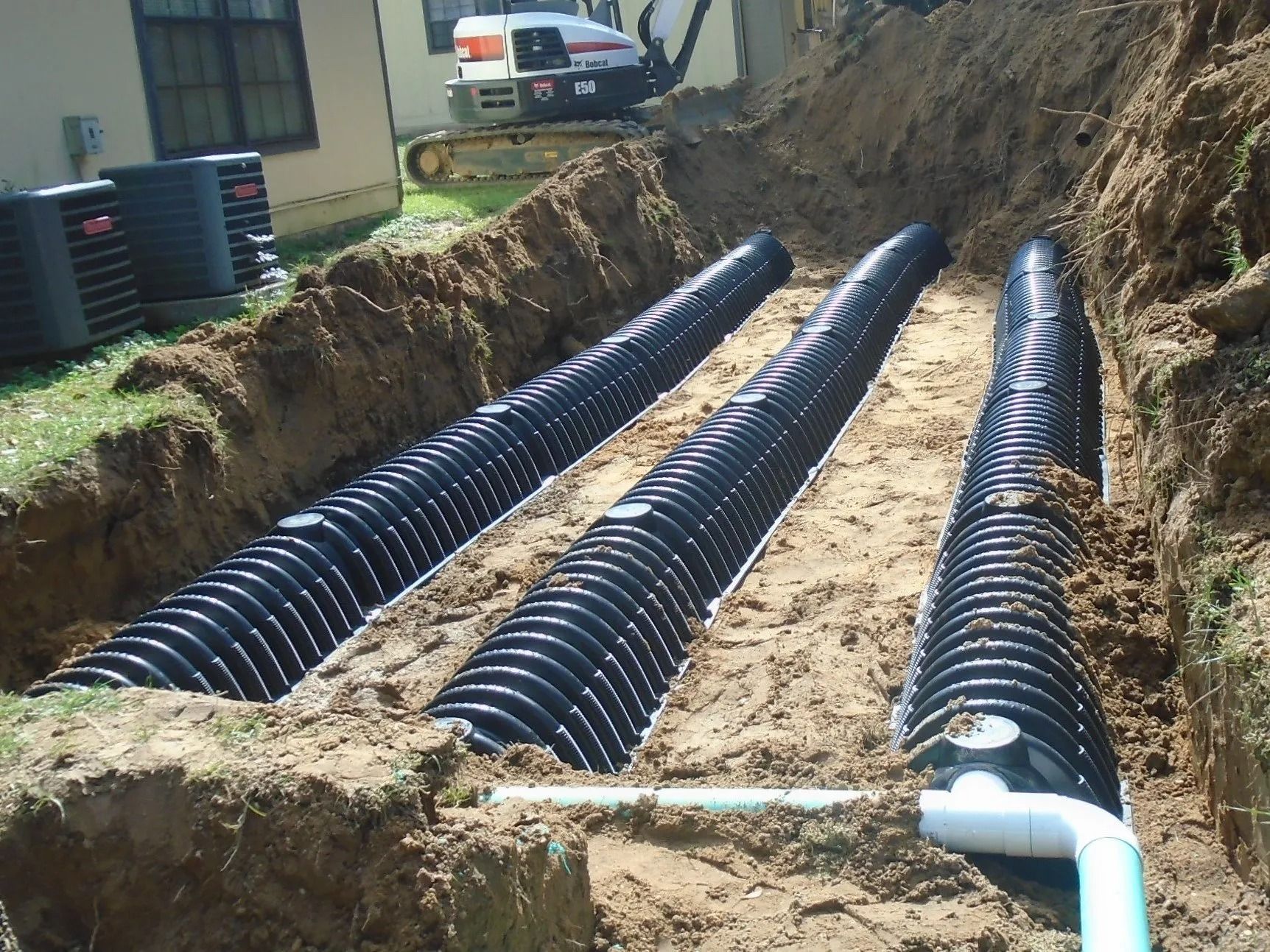 Three black corrugated pipes installed in trenches for a drainage system.