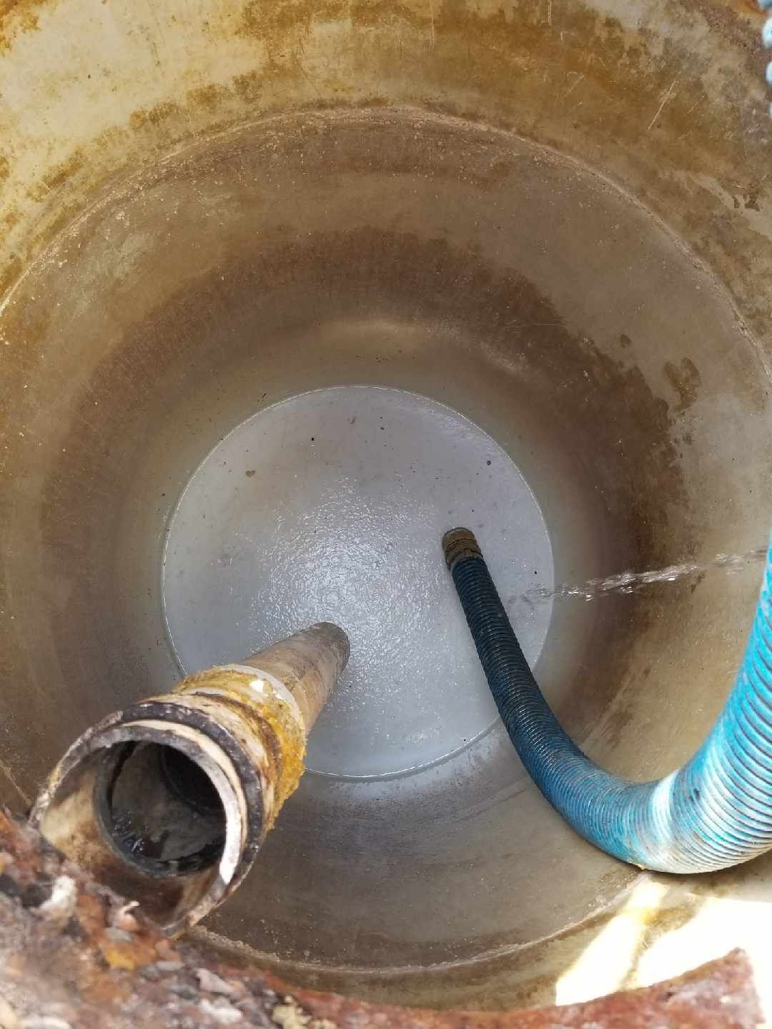 Inside a cylindrical, stained container with a rusty pipe and a blue hose spraying water.