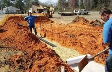 Men installing a drainage system in a construction site with equipment and piles of dirt.