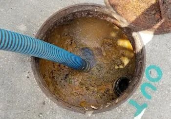 Open sewer with a blue hose inside, surrounded by brown sludge. Lid partially open.