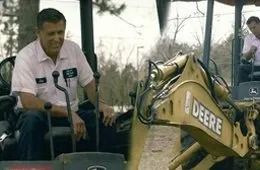 Man in a white shirt sits in an excavator. A second man is in the background operating machinery.