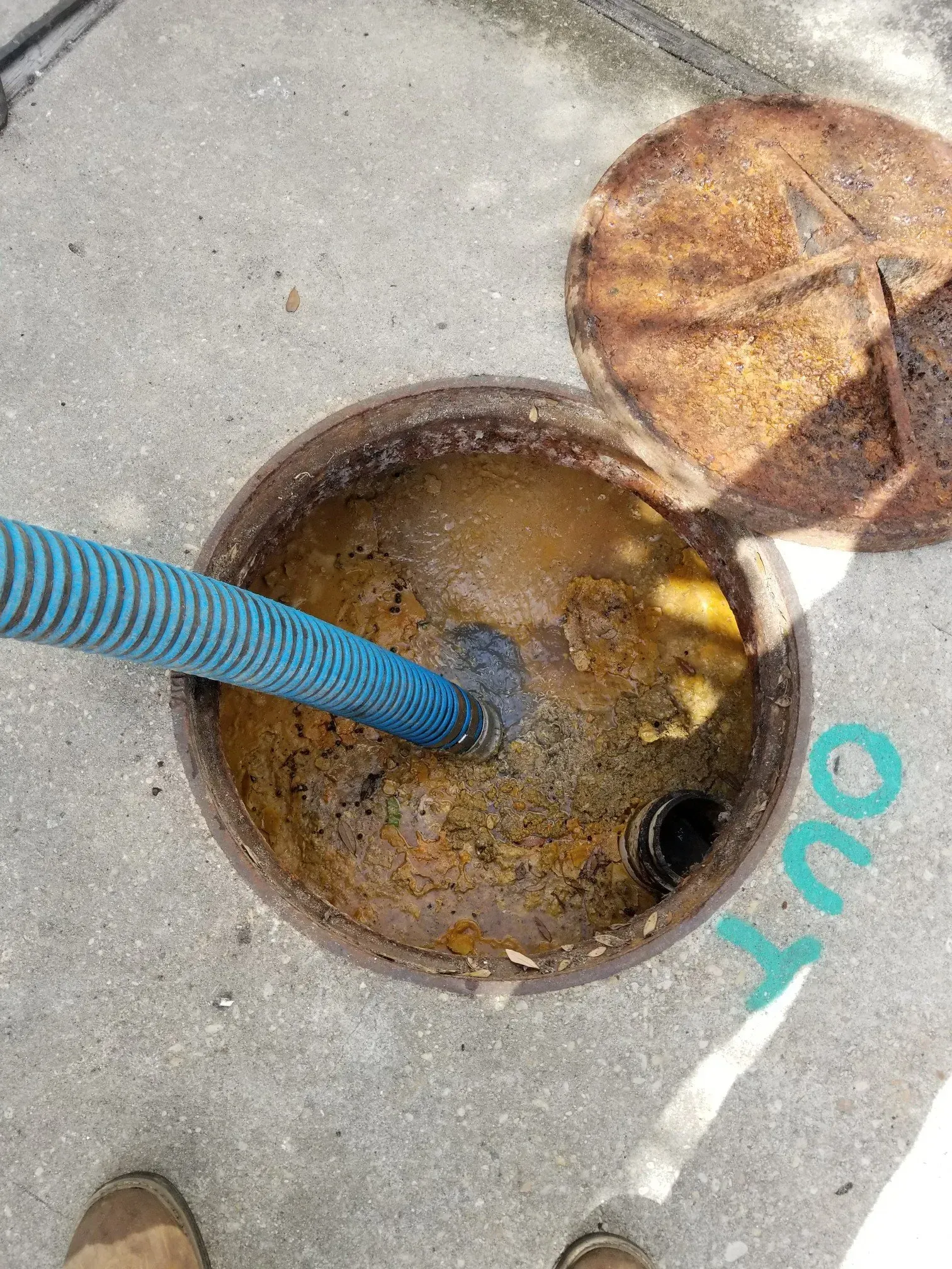 A rusty septic tank being pumped out with a blue hose. The open lid is next to it.
