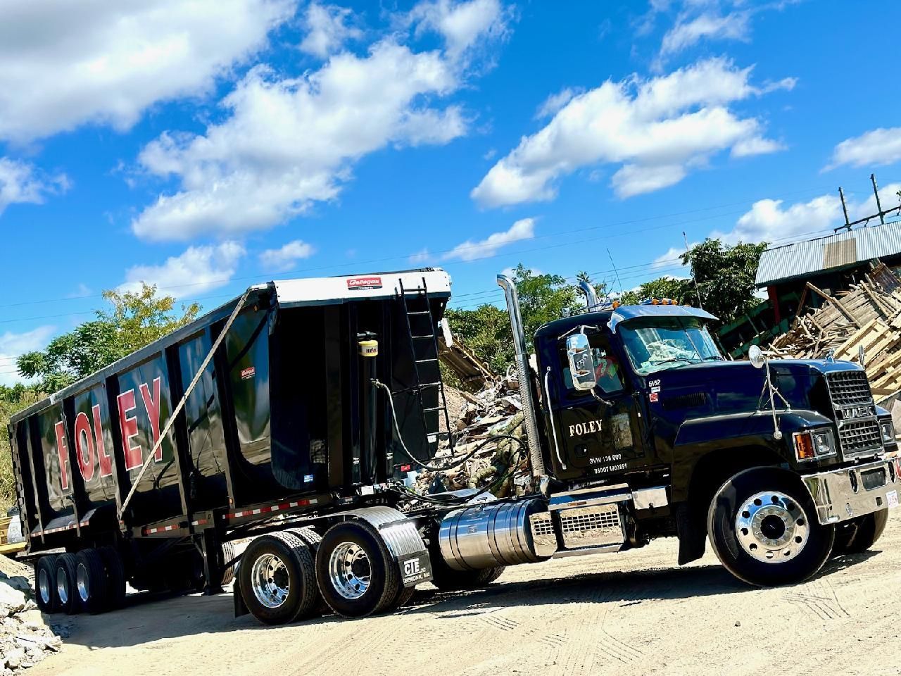 A dump truck with a trailer attached to it is parked on a dirt road.