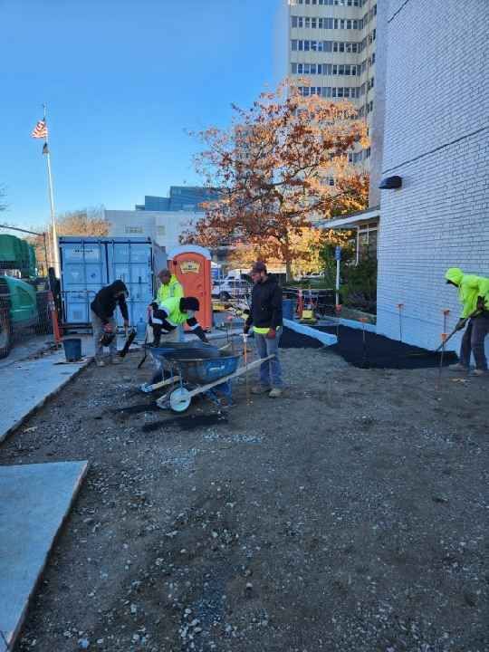 A group of construction workers are working on a sidewalk in front of a building.