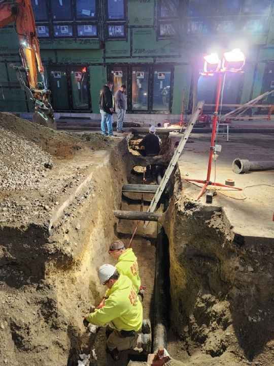 A group of construction workers are working on a pipe in a trench.