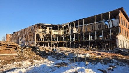 A large, multi-story brick industrial building with a collapsed interior section under a clear blue sky.