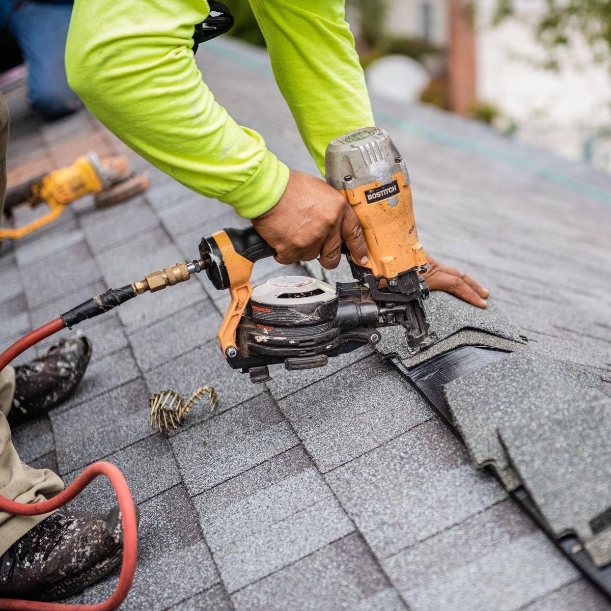 Worker using a nail gun to repair gray roof shingles