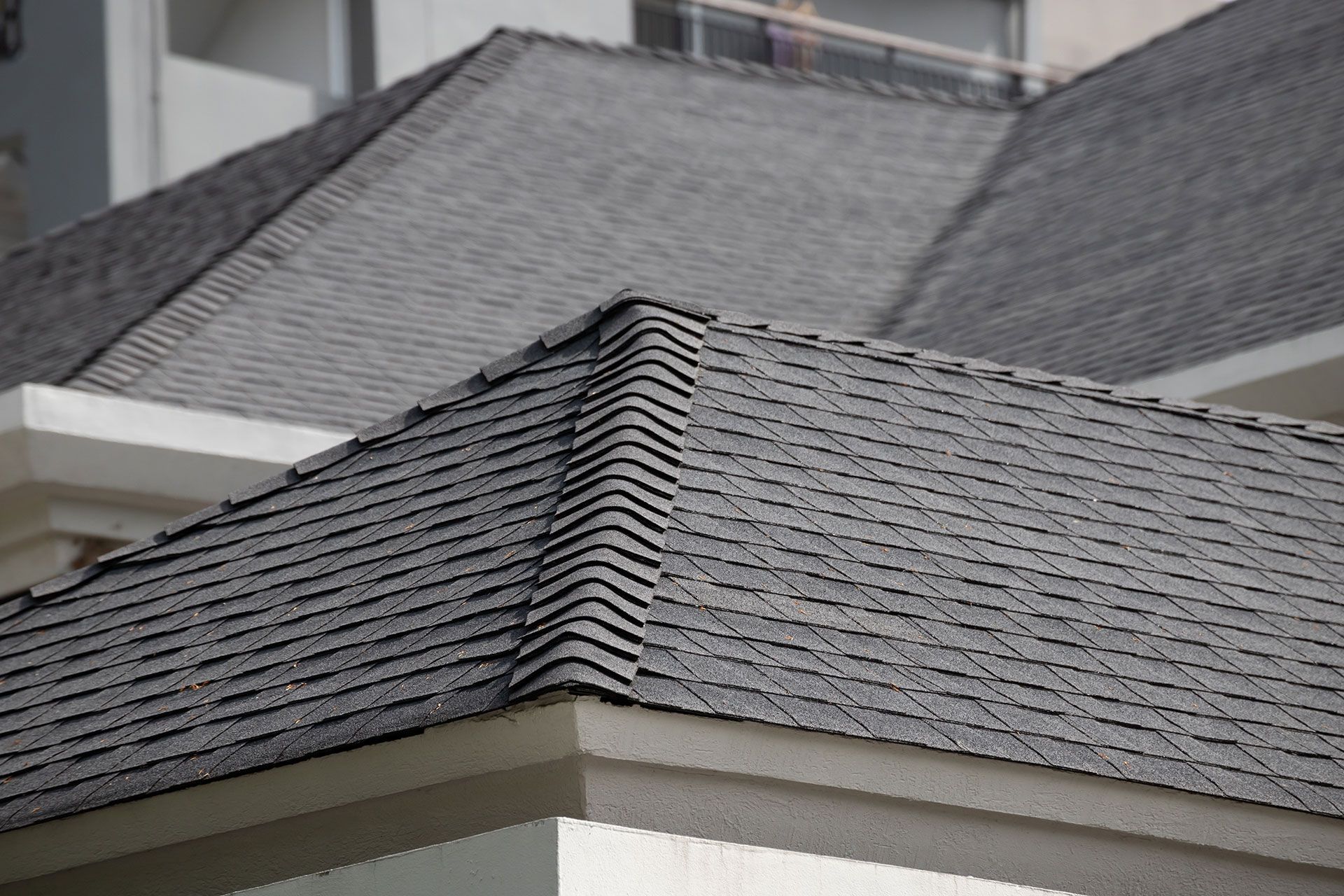 Close-up of a dark gray shingled roof with a light-colored building behind it